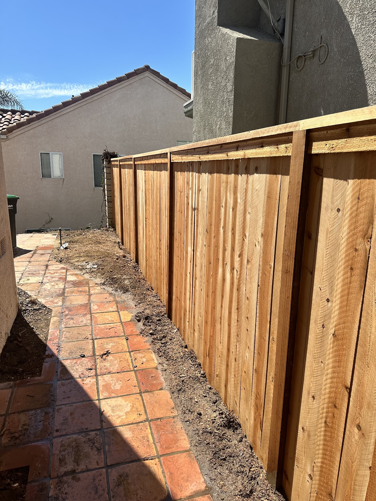 Freshly built redwood privacy fence beside a tiled walkway